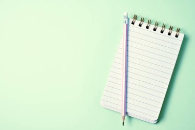 Pastel yeşil arkaplan üzerinde kalemler olan boş defterin üst görünümü 