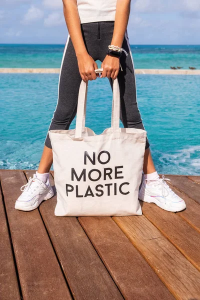 Gadis muda memegang tas eko katun dengan tanda Tidak Lebih Plastik pada biru tropis latar belakang laut — Stok Foto