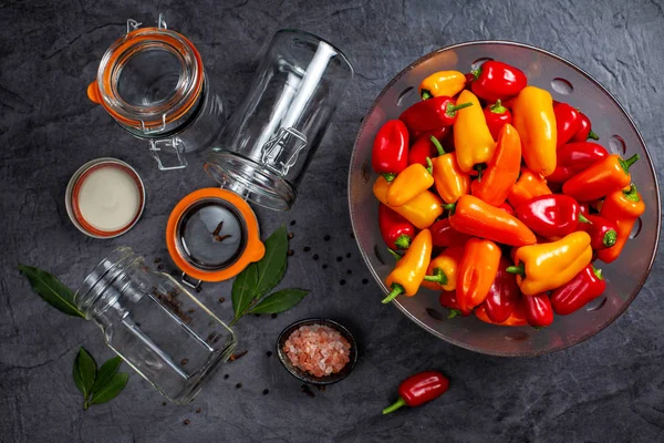 Colourful  mini bell peppers in glass bowl  and empty glass jars ready to be marinated on dark background, top view — Stock Photo, Image