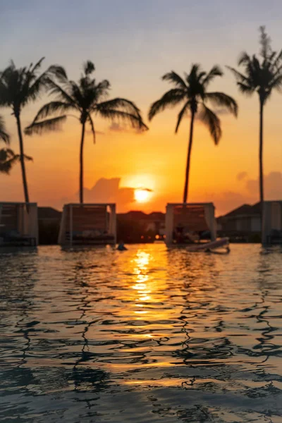 Orangefarbener tropischer Sonnenuntergang mit Reflexion des Poolwassers und Palmen im Hintergrund, selektiver Fokus, vertikale Komposition — Stockfoto