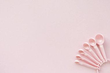 Pembe arka planda pembe renkli plastik kaşık ölçülüyor.