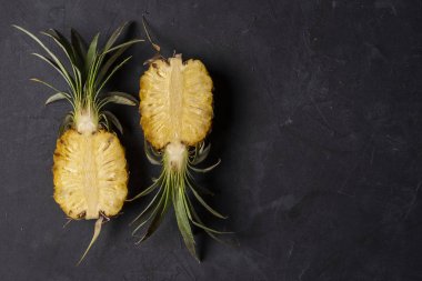 Siyah zemin üzerinde taze kesilmiş iki yarım ananas meyvesi, fotokopi alanı ile üst manzara 