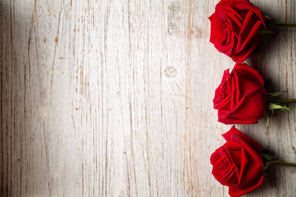 Три красные розы на светлом деревянном фоне с копировальным пространством, вид сверху - Изображение
