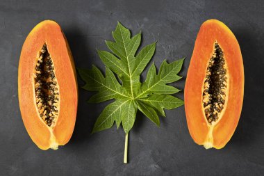 Olgun taze kesilmiş papaya meyvesi. Siyah arka planda yeşil papaya yaprağı. Üst manzara, kopyalama alanı. 
