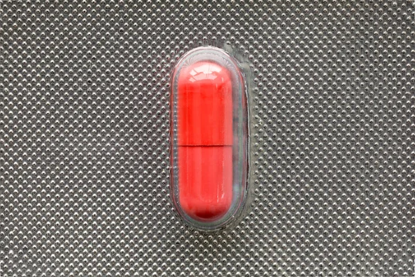 Single red medical  capsule in blister, macro, top view, medical concept