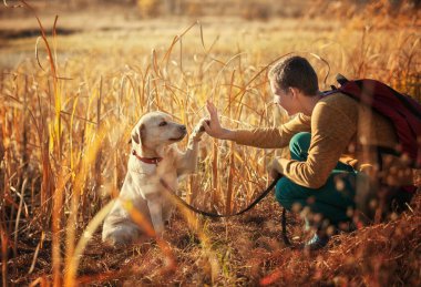 Genç çocuk köpeğiyle göl kenarında bir Labrador gezdiriyor.