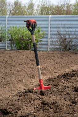 Kırmızı bir kürek yere saplanmış, kırmızı iş eldivenleri sapın üstünde asılı.