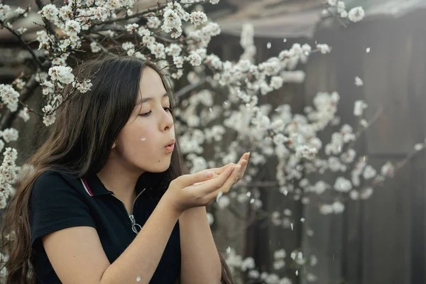 Saçı kiraz bahçesinde bir kız çalıların altında duruyor ve avucunun içinden kiraz yaprakları döküyor.