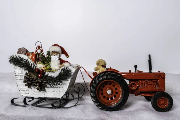 白いそりのサンタはクリスマスプレゼントでいっぱいです雪の中を赤いトラクターでテディベアで引きます — ストック写真