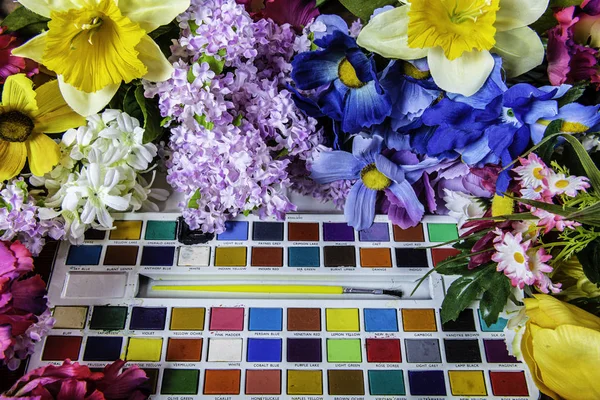 child's used paint set surrounded by colorful spring flowers