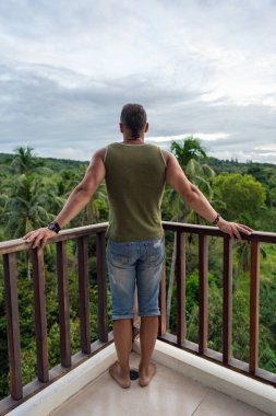 Yeşil t-shirt güçlü bir genç adam bir balkon tropikal ülkede tek başına duran