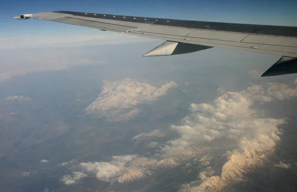 Montanhas e nuvens sob a asa de um avião — Fotografia de Stock