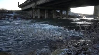 Köprünün altından hızlı su akışı. Icecicles sahilde ağacının dalları.