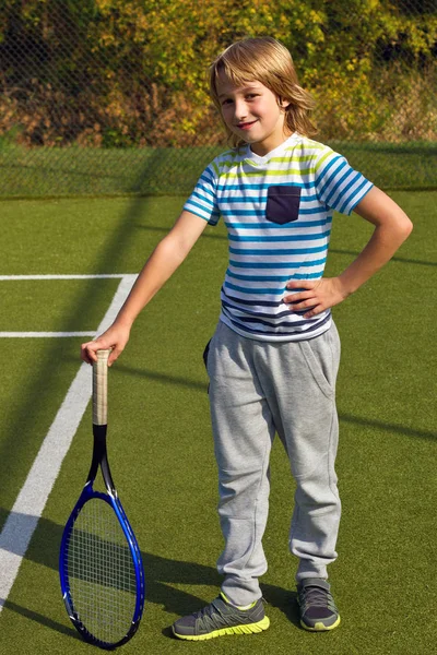 Niño de pie con raqueta de tenis y pelota en la cancha — Foto de Stock