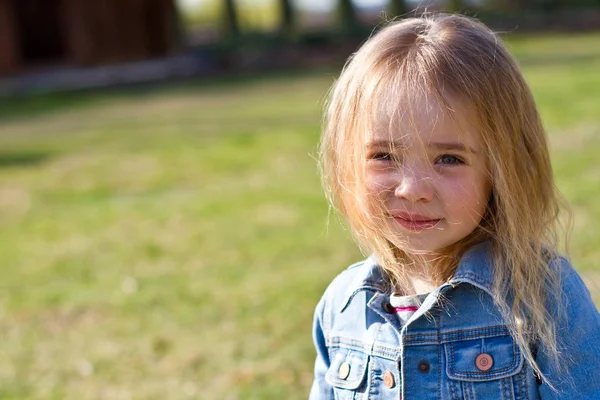 Beautiful charming little girl in jeans with disheveled hair on a background of green — Stock Photo, Image