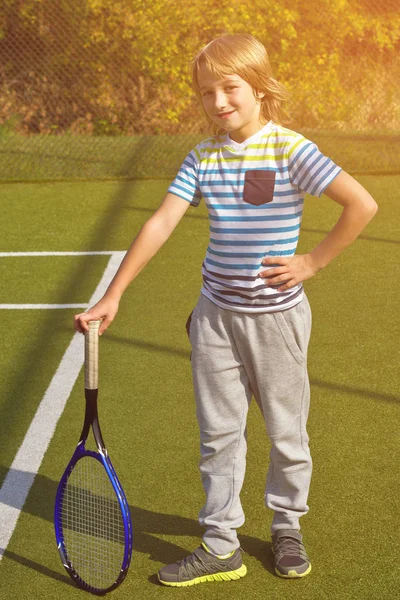 Niño de pie con raqueta de tenis y pelota en la cancha —  Fotos de Stock