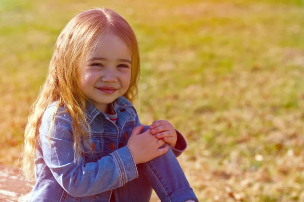 Vackra charmiga lilla flicka i jeans med rufsig hår på en bakgrund av grön — Stockfoto