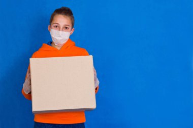 Mavi stüdyo arka planında boş karton kutu taşıyan yüz eldivenleri dağıtan işçi maskesi Coronavirus virüsü salgını karantina 2019 nk konsepti.