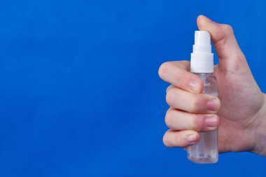 İnsan elleri sprey, dezenfektan, baloncukta antiseptik, mavi arka planda kavanoz kullanır..