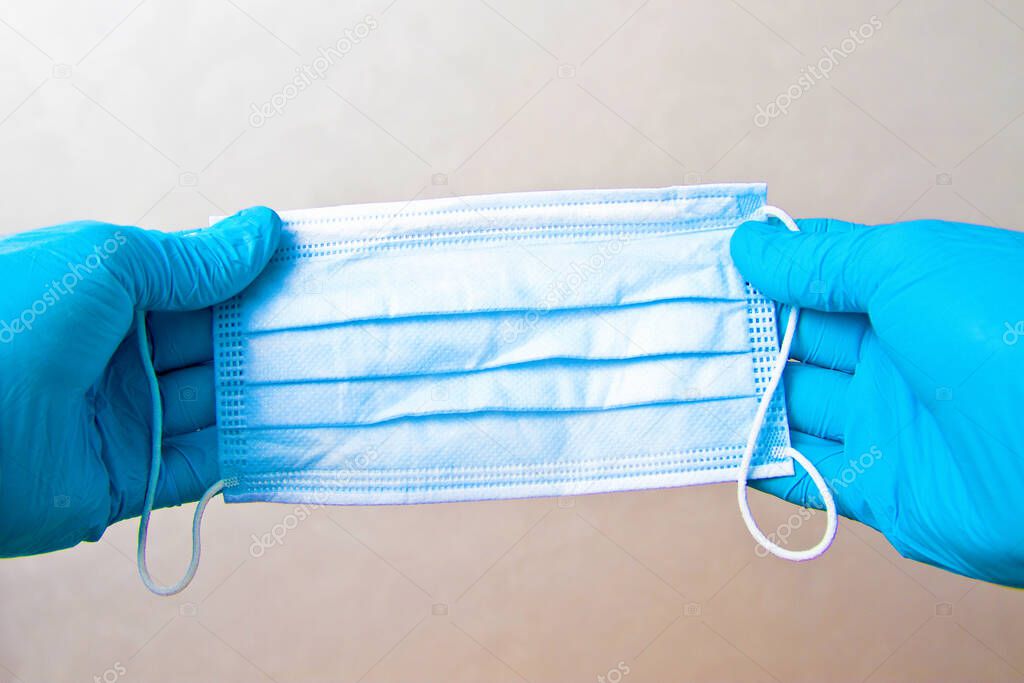 Man hands in blue disposable gloves holding medicine face mask on gray background. Emergency medical care