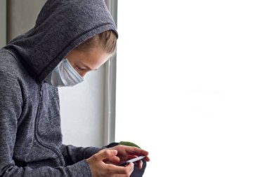 Koronavirüsü karantinaya alırken, yüzü maskeli bir çocuk pencerede oturuyor..