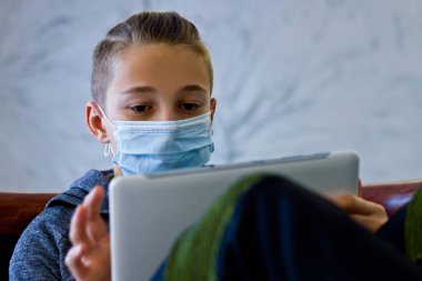 Çocuk evde karantina sırasında maske takmış oturuyor.