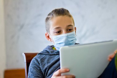 Çocuk evde karantina sırasında maske takmış oturuyor.