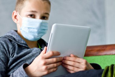 Çocuk evde karantina sırasında maske takmış oturuyor..