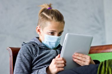 Çocuk evde karantina sırasında maske takmış oturuyor..