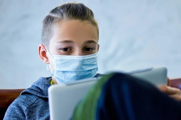 Boy sitting with tablet in mask during quarantine at home