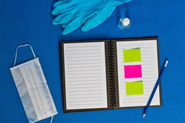 Lastik eldiven dezenfektanı ve yüz maskesi ile test tüpü bir defter üzerinde ve mavi bir arka planda yatıyor