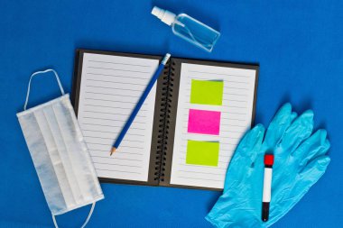 Lastik eldiven dezenfektanı ve yüz maskesi ile test tüpü bir defter üzerinde ve mavi bir arka planda yatıyor
