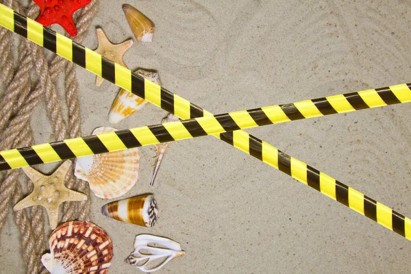 Barrier tape - quarantine, isolation, entry ban. Summer flat composition with seashells, rope, sand beach and space for text on sandy background.