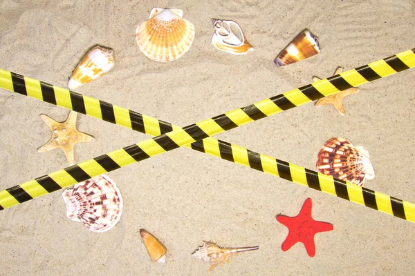 Barrier tape - quarantine, isolation, entry ban. Seashells and nautical rope decoration on sand background with red toy ship.