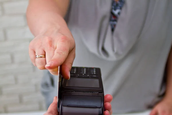 A female hand holds a card through the terminal to pay for the goods.