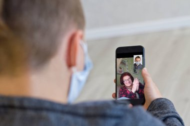 Videoda gülümseyen yaşlı bir büyükanneyle konuşan bir adamın görüntüsü. Evde karantinada mutlu bir büyükanneyle iletişim kurmak için mobil bir cihaz kullanan bir torun..