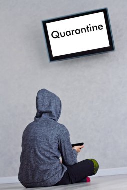 Çocuk, koronavirüs karantinası sırasında telefonuyla karantinaya alınan televizyonun yanında oturuyor.