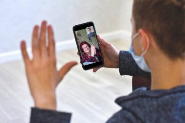 Videoda gülümseyen yaşlı bir büyükanneyle konuşan bir adamın görüntüsü. Evde karantinada mutlu bir büyükanneyle iletişim kurmak için mobil bir cihaz kullanan bir torun..