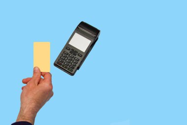 El ödeme terminalinde bir kredi kartı tutuyor. Mavi arkaplanda izole.