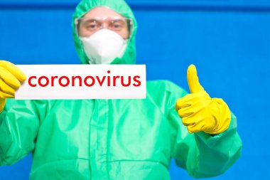 Üzerinde mavi arka planda duran beyaz bir afiş taşıyan Coronavirus yazan bir sağlık görevlisi..