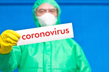 Üzerinde mavi arka planda duran beyaz bir afiş taşıyan Coronavirus yazan bir sağlık görevlisi..