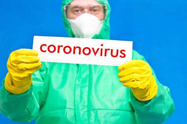 Üzerinde mavi arka planda duran beyaz bir afiş taşıyan Coronavirus yazan bir sağlık görevlisi..