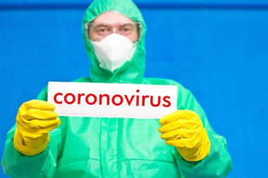 Üzerinde mavi arka planda duran beyaz bir afiş taşıyan Coronavirus yazan bir sağlık görevlisi..