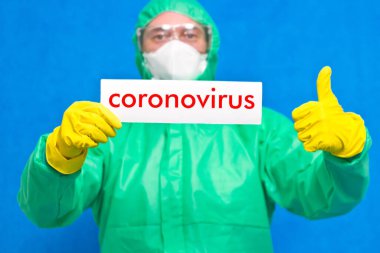 Üzerinde mavi arka planda duran beyaz bir afiş taşıyan Coronavirus yazan bir sağlık görevlisi..
