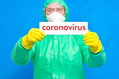 Üzerinde mavi arka planda duran beyaz bir afiş taşıyan Coronavirus yazan bir sağlık görevlisi..