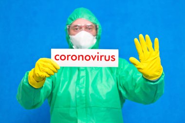 Üzerinde mavi arka planda duran beyaz bir afiş taşıyan Coronavirus yazan bir sağlık görevlisi..