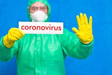 Üzerinde mavi arka planda duran beyaz bir afiş taşıyan Coronavirus yazan bir sağlık görevlisi..