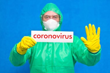 Üzerinde mavi arka planda duran beyaz bir afiş taşıyan Coronavirus yazan bir sağlık görevlisi..