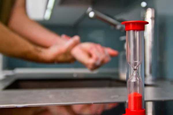 Man washes his hands with soap and uses an hourglass to measure hand washing time.