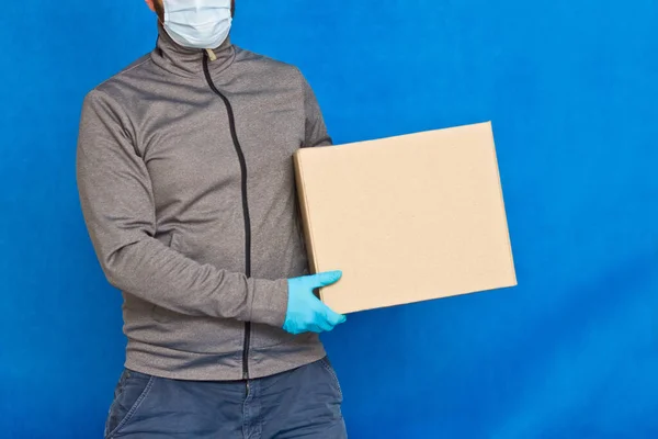Courier Hand Holds Brown Box Blue Background Rubber Gloves Face — Stock Photo, Image
